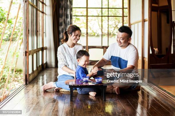 japanese woman, man and little boy sitting on floor on porch of traditional japanese house, drinking tea. - the japanese wife - fotografias e filmes do acervo