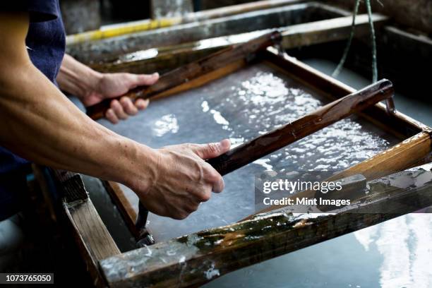 japanese man in a workshop, holding a wooden frame with pressed pulp, making traditional washi paper. - 手漉きの紙 ストックフォトと画像