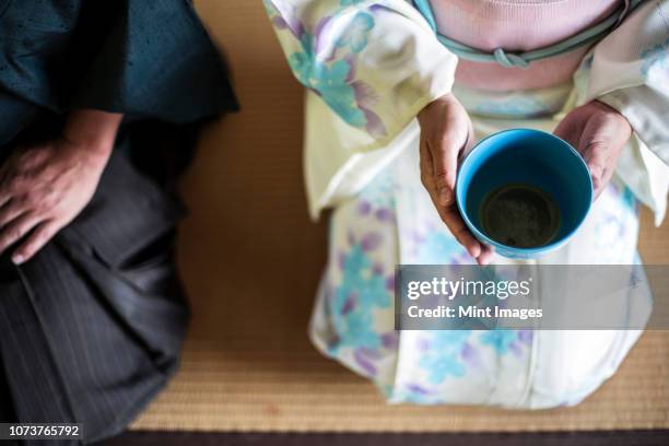 high angle close up of japanese man and woman wearing traditional white kimono with blue floral pattern kneeling on floor during tea ceremony, holding blue tea bowl. - tea ceremony stock-fotos und bilder