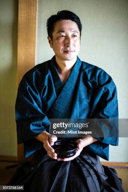 japanese man wearing kimono kneeling on floor, holding tea bowl during tea ceremony. - kimono stock pictures, royalty-free photos & images
