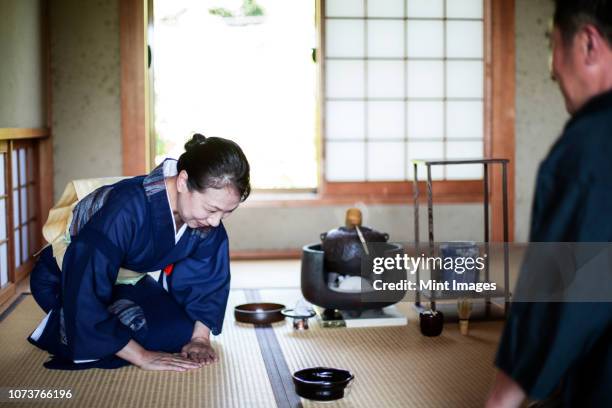 japanese woman wearing traditional bright blue kimono with cream coloured obi and man kneeling on floor during tea ceremony. - teceremoni bildbanksfoton och bilder