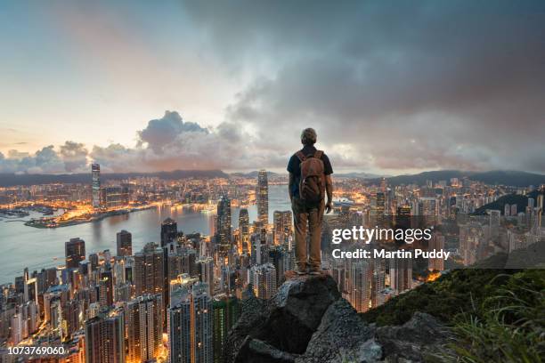 a man standing on a rock overlooking hong kong skyline at dawn, from victoria peak - power supply - fotografias e filmes do acervo