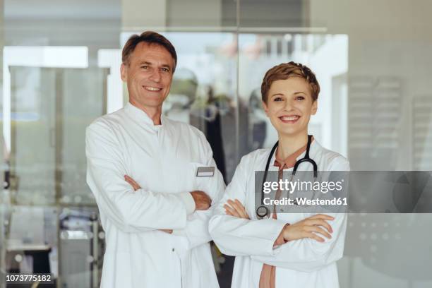 two confident doctors standing in practice, with arms crossed - doctor with arms crossed stock pictures, royalty-free photos & images