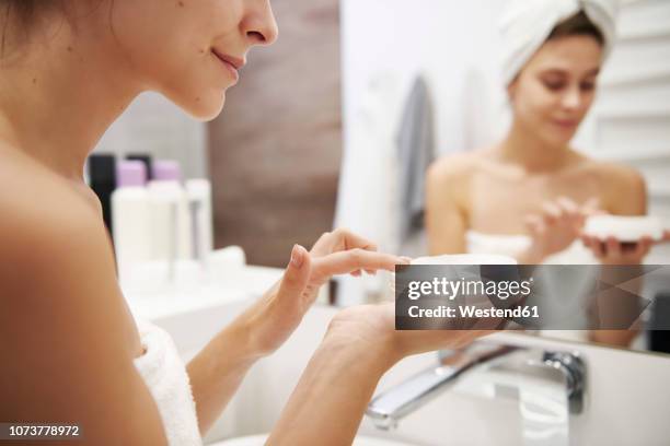 young woman applying moisturizer in bathroom, partial view - cremas faciales fotografías e imágenes de stock