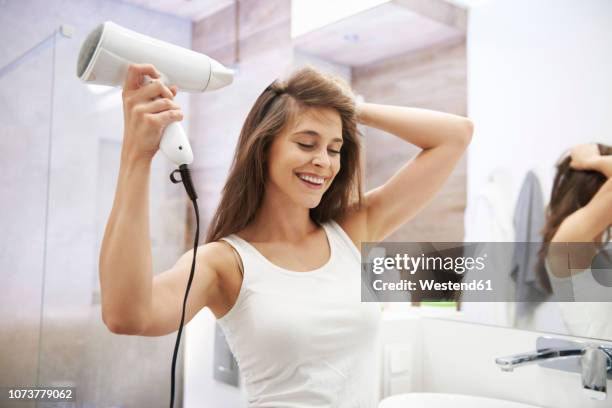 portrait of laughing woman using hair dryer in the bathroom - secador de cabelo - fotografias e filmes do acervo