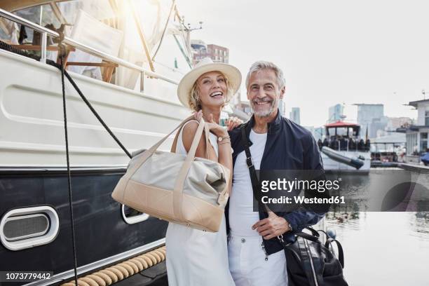 older man and young woman standing with travelling bags on jetty next to yacht - older couple travelling photos et images de collection
