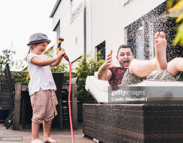 fathercand daughter in the garden, daughter splashing water with hose - water garden fotografías e imágenes de stock