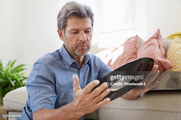 mature man at home sitting in front of couch, looking at old vinyl record - looking at a photo album stock-fotos und bilder