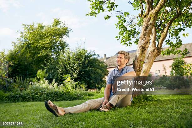 mature man standing in his garden wearing apron - mann lässig gras sitzen stock-fotos und bilder