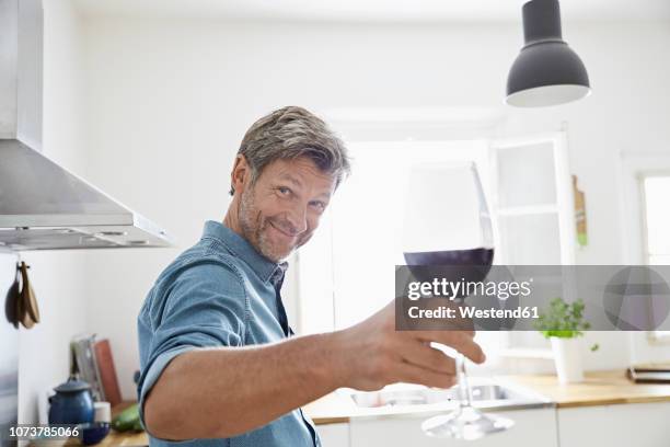 man in kitchen toasting with glass of red wine - men drinking wine foto e immagini stock