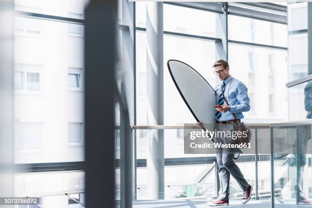 businessman with cell phone carrying surfboard in office - afterwork stock pictures, royalty-free photos & images