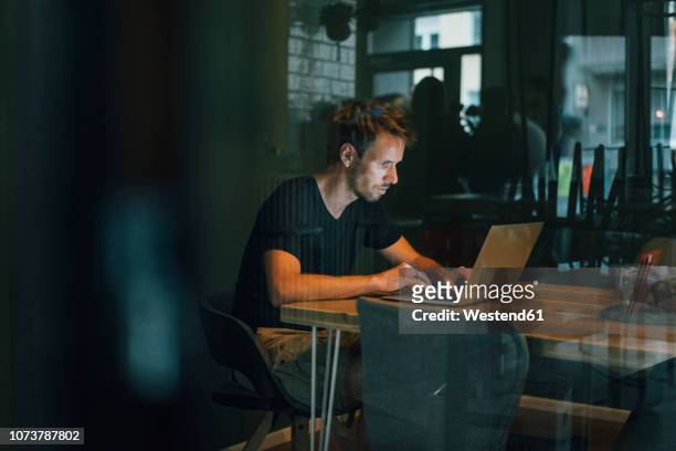 man sitting in office, working late in his start-up company - internet café stock-fotos und bilder