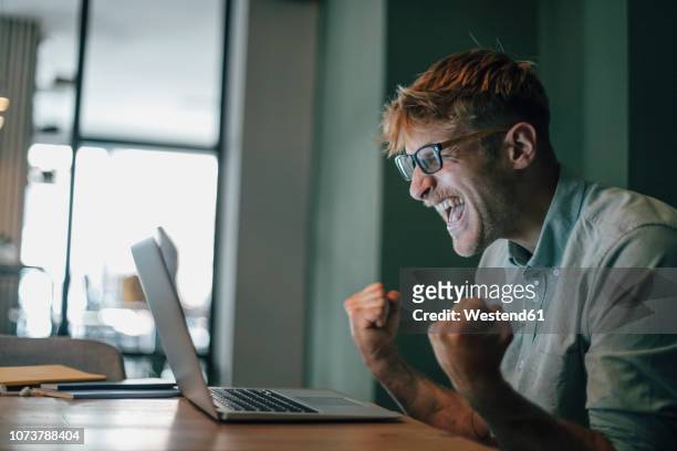 young man using laptop, laughing happly - vincere foto e immagini stock