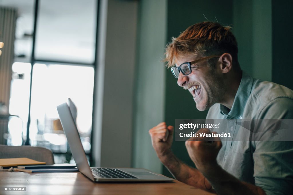 Young man using laptop, laughing happly