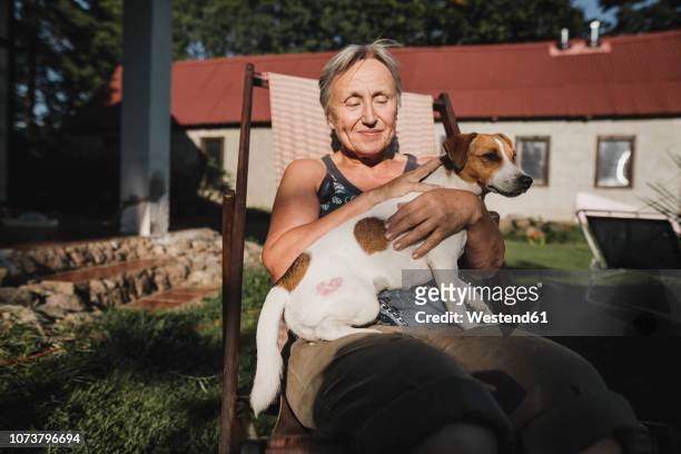smiling senior woman with dog on deckchair in garden - haustierbesitzer stock-fotos und bilder