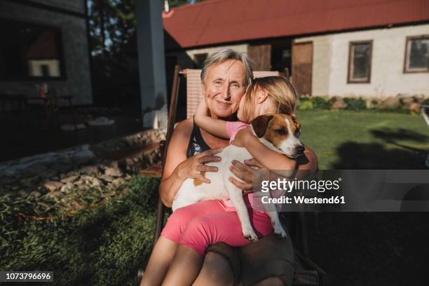 smiling grandmother with granddaughter and dog on deckchair in garden - family dog stock-fotos und bilder