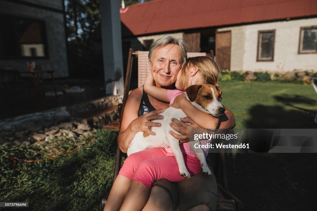 Smiling grandmother with granddaughter and dog on deckchair in garden