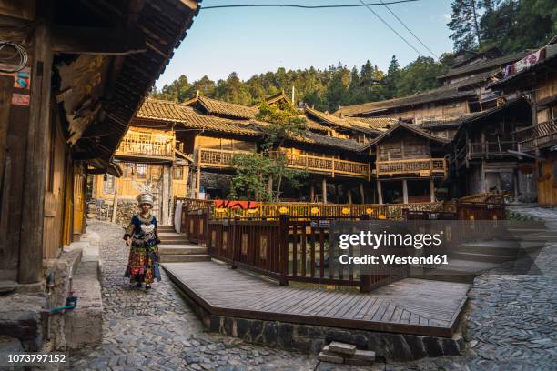 china, guizhou, young miao woman in traditional dress walking in a settlement - tribal head gear in china stock pictures, royalty-free photos & images