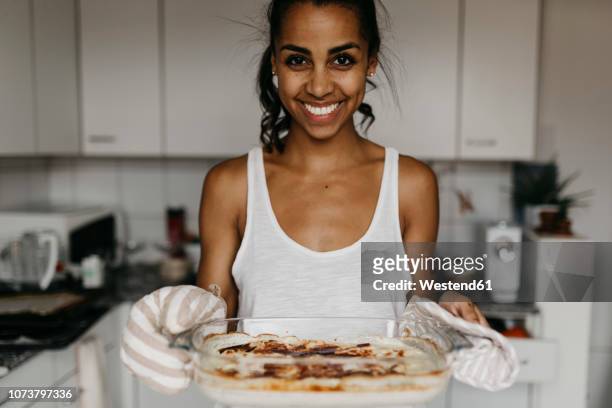portrait of smiling young woman with casserole in the kitchen - casserole stock pictures, royalty-free photos & images