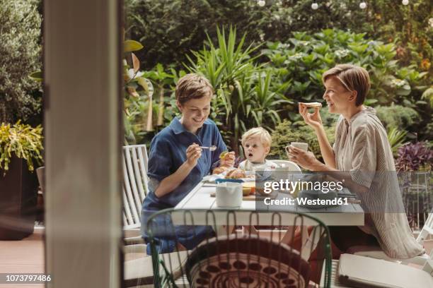 two happy mothers at breakfast table outdoors with their child - breakfast family stock-fotos und bilder