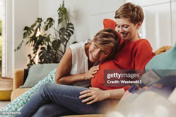 happy lesbian couple feeling movements of baby belly of the expectant mother - lifestyle moments stockfoto's en -beelden