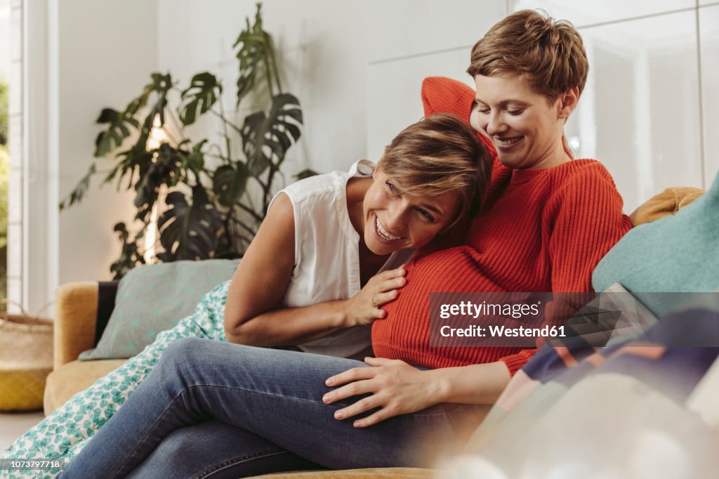 Happy lesbian couple feeling movements of baby belly of the expectant mother