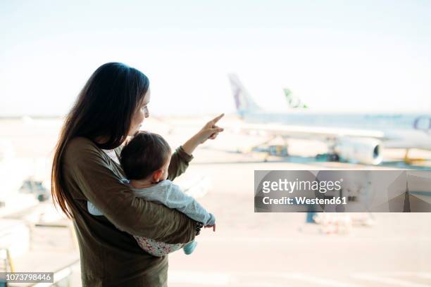 mother holding a baby girl at the airport, pointing at the airplanes - baby pointing stock pictures, royalty-free photos & images