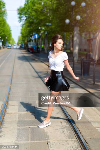 young woman crossing a street with tramway tracks in the city - windy skirt 個照片及圖片檔