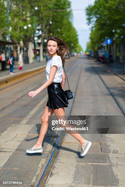 young woman crossing a street with tramway tracks in the city - skirt blowing ストックフォトと画像