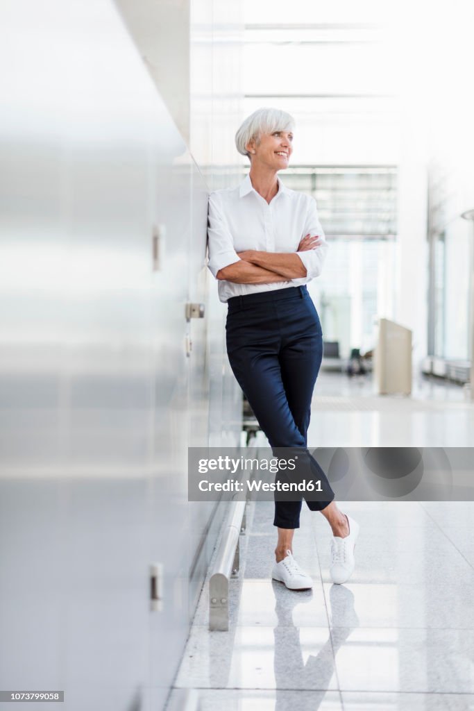 Smiling senior businesswoman leaning against a wall