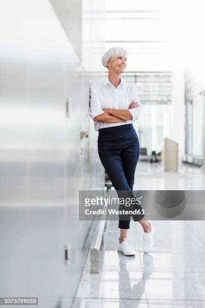 smiling senior businesswoman leaning against a wall - lean imagens e fotografias de stock