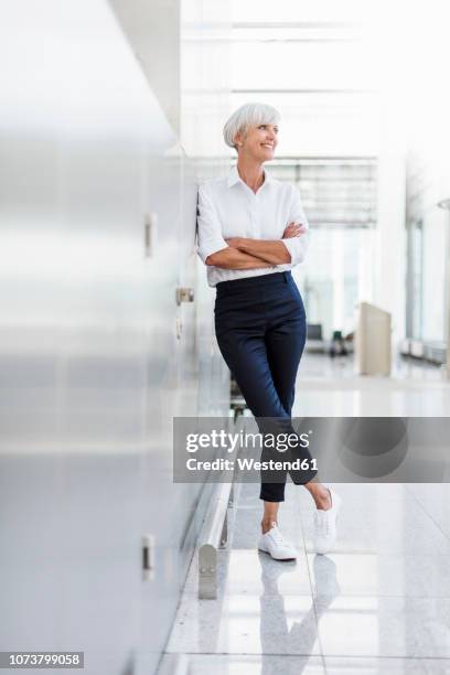 smiling senior businesswoman leaning against a wall - luta fysisk ställning bildbanksfoton och bilder