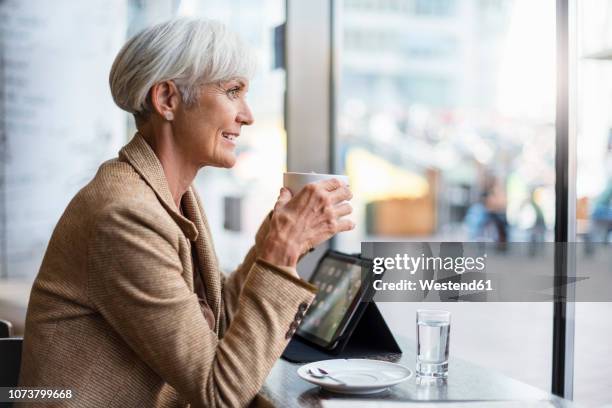 smiling senior businesswoman with tablet in a cafe - brown coat stock pictures, royalty-free photos & images