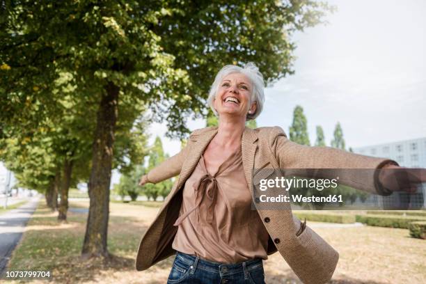 happy senior woman with outstretched arms in a park - drehen stock-fotos und bilder