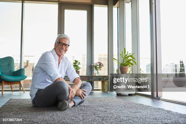 smiling mature man relaxing sitting on carpet at home - sitting on the floor stock-fotos und bilder