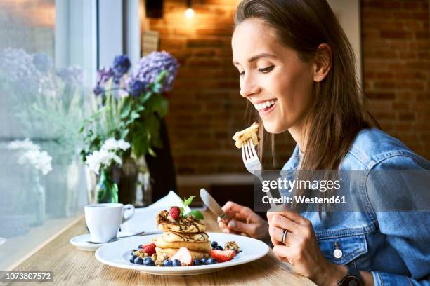 smiling young woman eating pancakes in cafe - breakfast restaurant stock pictures, royalty-free photos & images