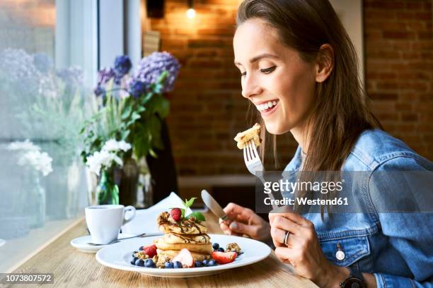 smiling young woman eating pancakes in cafe - plate eating table imagens e fotografias de stock