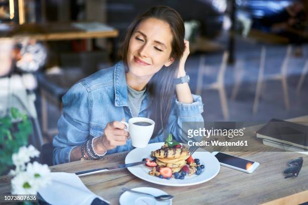 smiling young woman enjoying pancakes and coffee in cafe - crepe textile fotografías e imágenes de stock