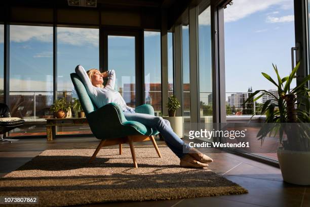 mature woman relaxing in armchair in sunlight at home - build wealth stockfoto's en -beelden