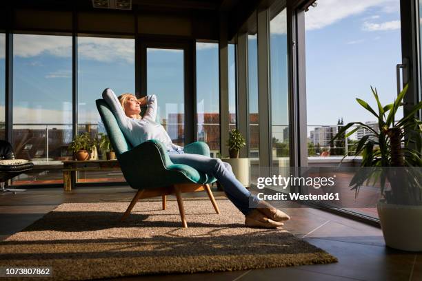 mature woman relaxing in armchair in sunlight at home - perfect home stock pictures, royalty-free photos & images