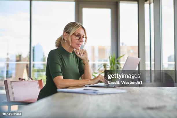 mature woman using laptop on table at home - groene jurk stockfoto's en -beelden
