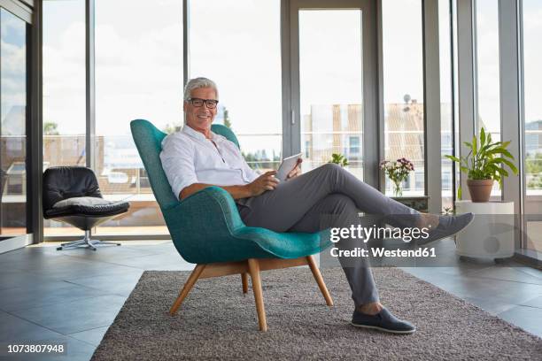 portrait of mature man sitting in armchair at home holding tablet - entry draft portraits foto e immagini stock