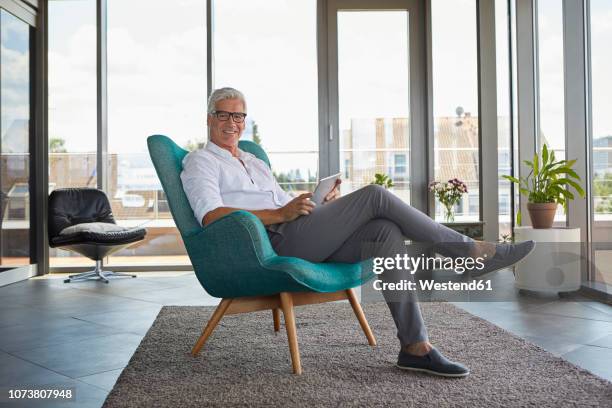 portrait of mature man sitting in armchair at home holding tablet - entry draft portraits stock pictures, royalty-free photos & images