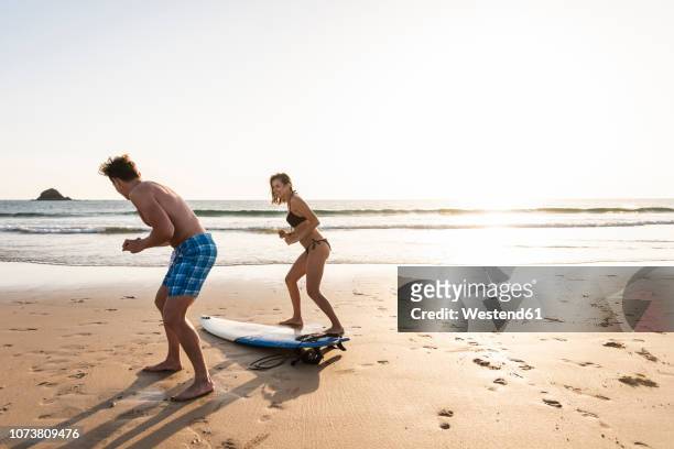 young man showing young woman how to surf on the beach - passenger train stockfoto's en -beelden