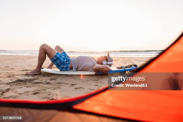 young surfer relaxing on the beach, listening music - beach music stock pictures, royalty-free photos & images