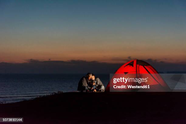 romantic couple camping on the beach, using smartphone - zelt nacht stock-fotos und bilder