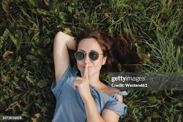 portrait of smiling woman wearing sunglasses lying in grass - woman mouth stock-fotos und bilder