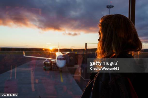 young woman looking through window on plane at the airport at sunset - aeroplano foto e immagini stock