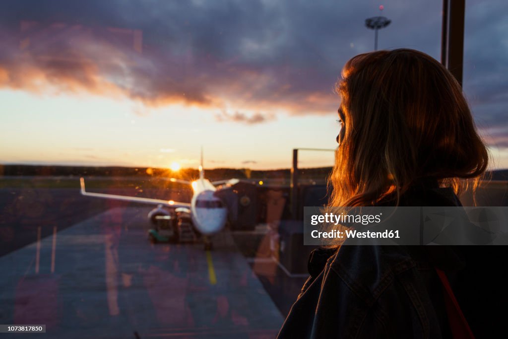 Young woman looking through window on plane at the airport at sunset