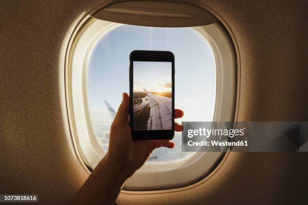 hand taking cell phone picture out of plane window - plane wing stock-fotos und bilder